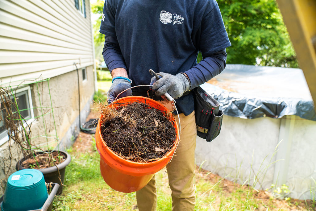 gutter services - cleaning - tech holding a bucket of debris from gutters