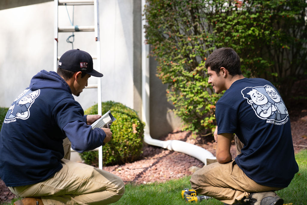 gutter installation services - techs evaluating the downspout of a gutter system